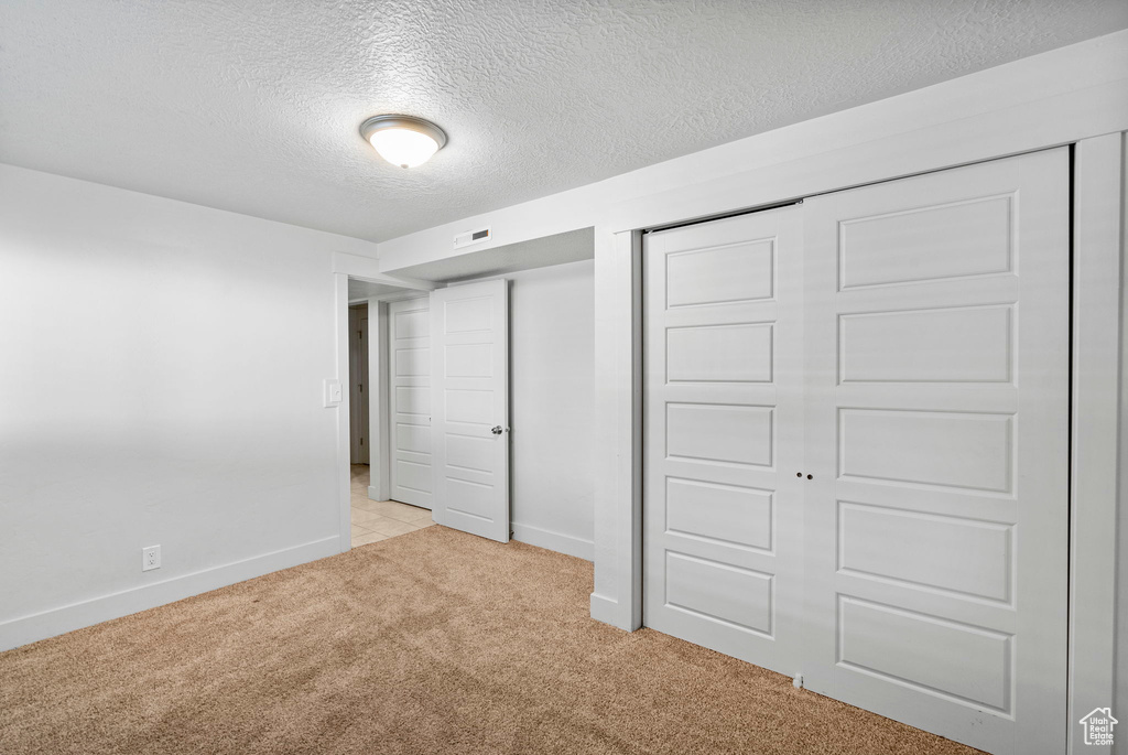 Unfurnished bedroom featuring baseboards, a textured ceiling, and light carpet