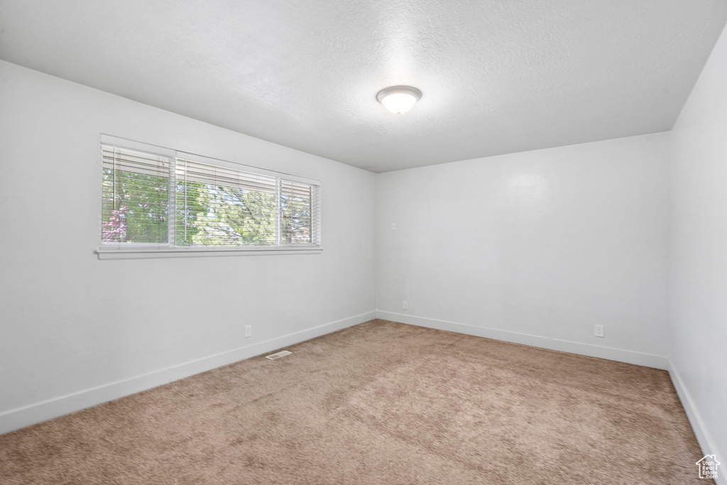 Unfurnished room featuring baseboards, light colored carpet, a textured ceiling, and visible vents