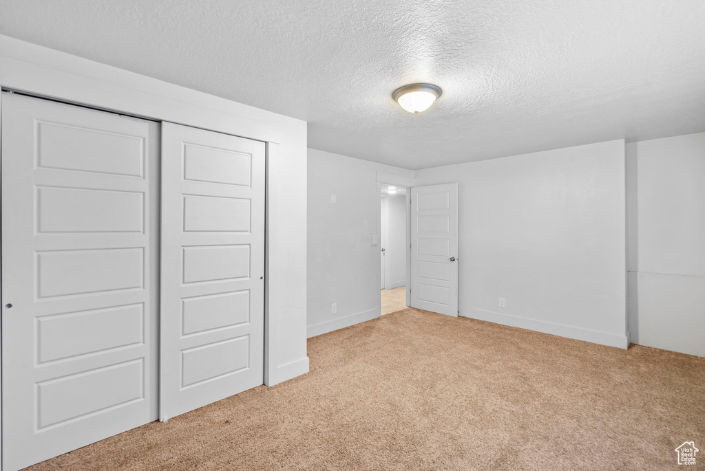 Unfurnished bedroom featuring a textured ceiling, baseboards, carpet, and a closet