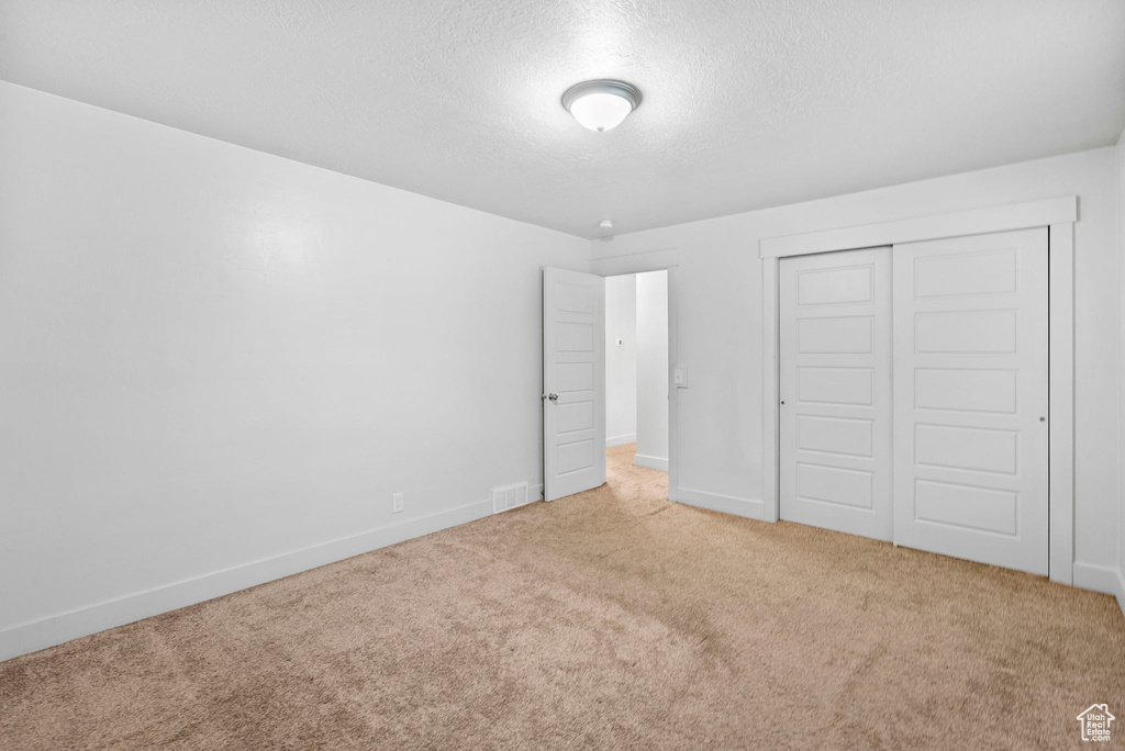 Unfurnished bedroom featuring a textured ceiling, carpet, baseboards, visible vents, and a closet