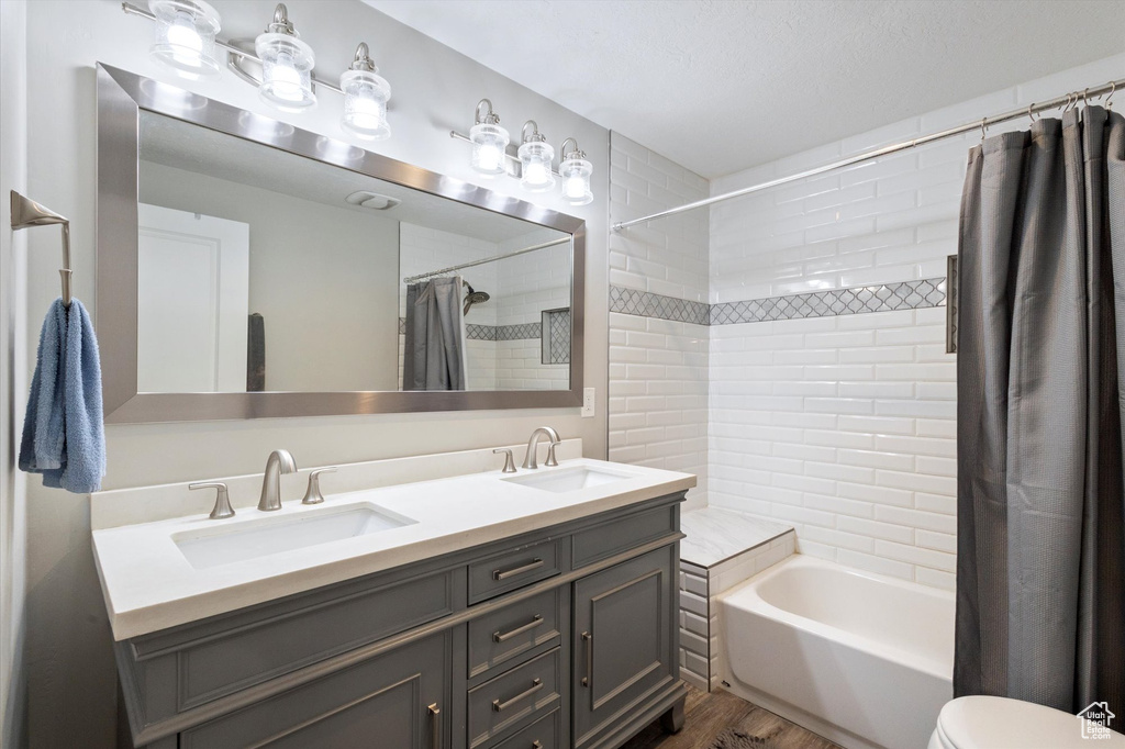 Bathroom with double vanity, a sink, shower / tub combo, and wood finished floors