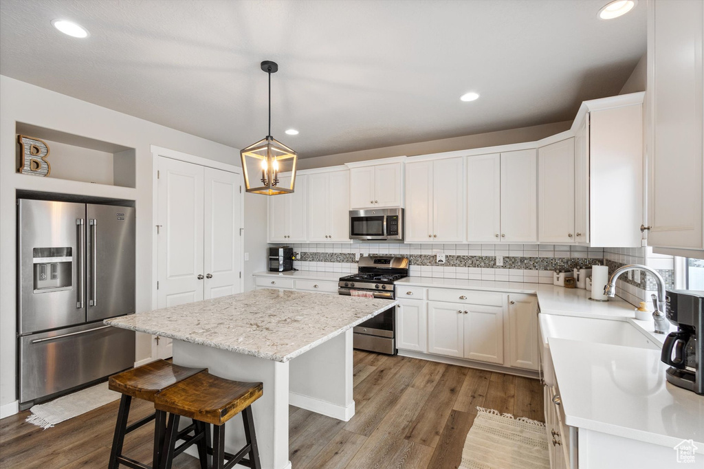 Kitchen with a kitchen island, appliances with stainless steel finishes, tasteful backsplash, a sink, and light wood-style flooring