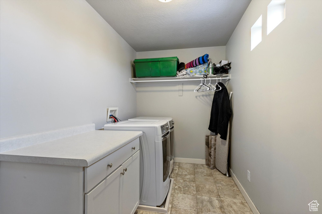 Clothes washing area with baseboards, cabinet space, and washer and dryer