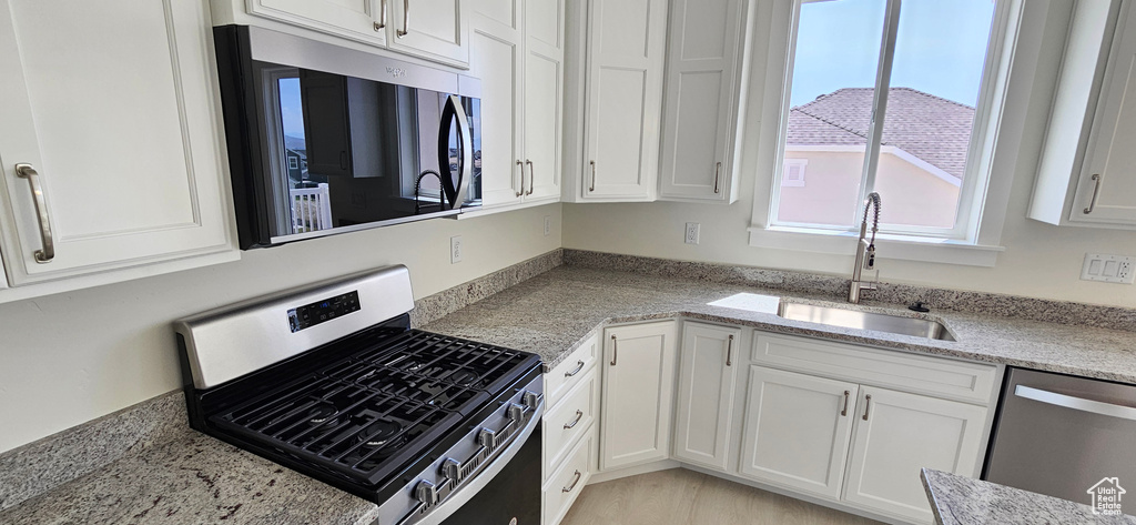 Kitchen with appliances with stainless steel finishes, white cabinetry, and light stone counters