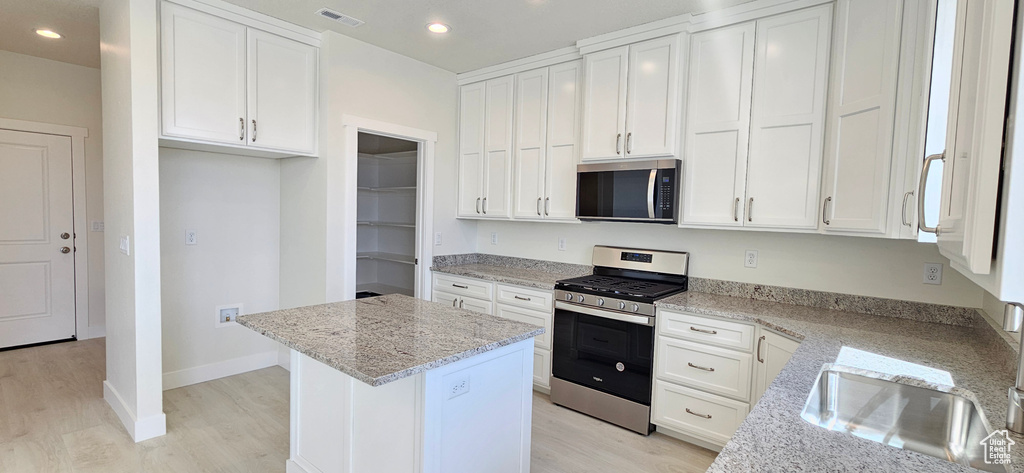 Kitchen with appliances with stainless steel finishes, light wood-type flooring, light stone countertops, white cabinetry, and recessed lighting