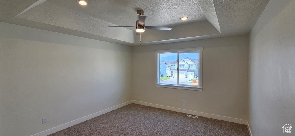 Carpeted empty room with a textured ceiling, ceiling fan, a raised ceiling, and recessed lighting
