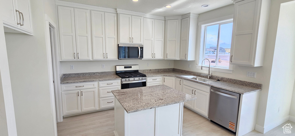 Kitchen with appliances with stainless steel finishes, a center island, white cabinets, light stone countertops, and light wood-style flooring