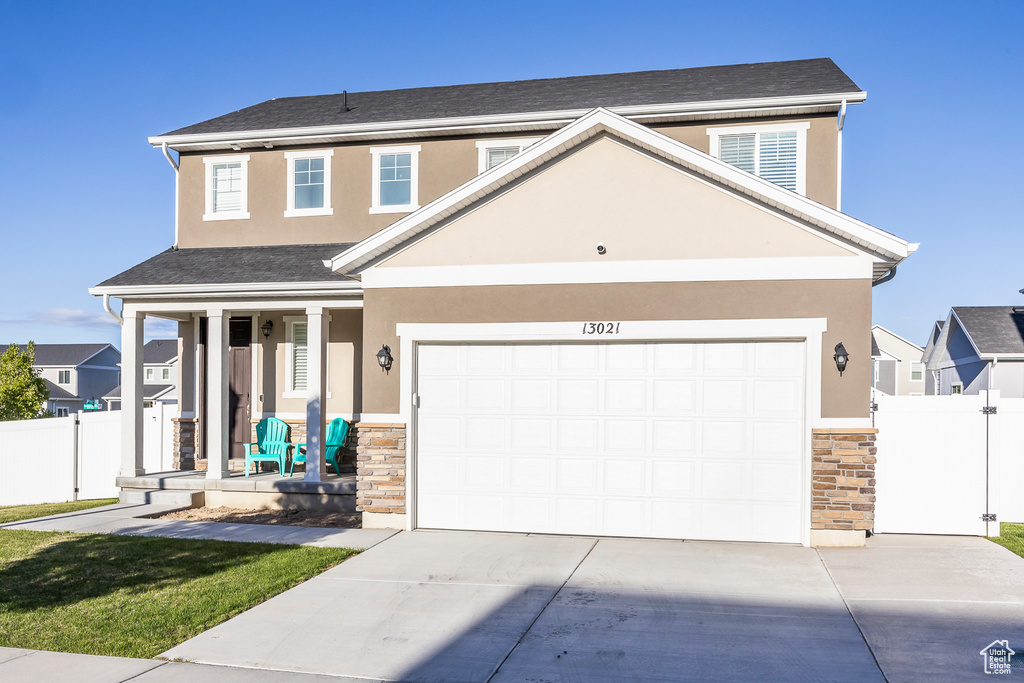 Traditional-style home featuring a porch, fence, driveway, and stone siding