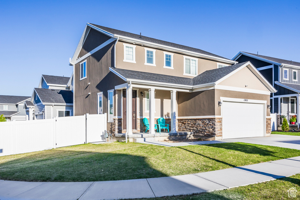 View of front of property with a front lawn, fence, covered porch, stone siding, and concrete driveway