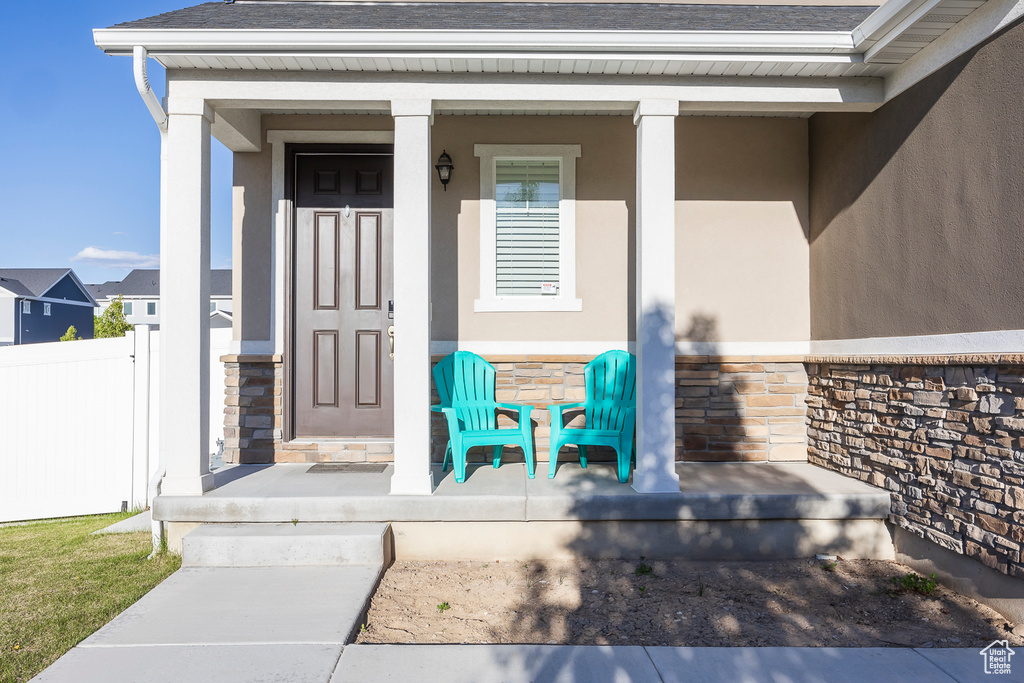 Entrance to property with fence, covered porch, stone siding, roof with shingles, and stucco siding