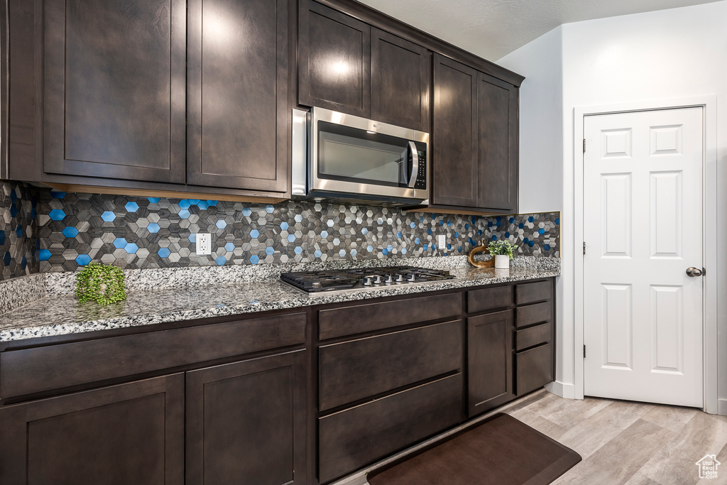 Kitchen with light stone counters, dark brown cabinetry, stainless steel appliances, and light wood-type flooring