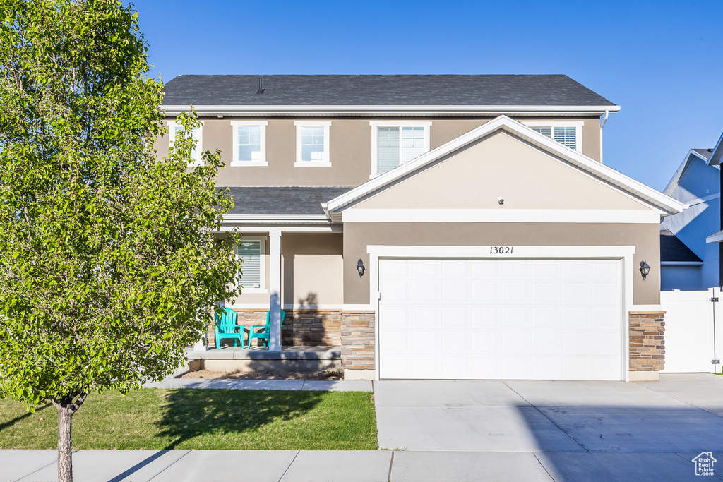 View of front of property with a garage, stucco siding, driveway, and stone siding