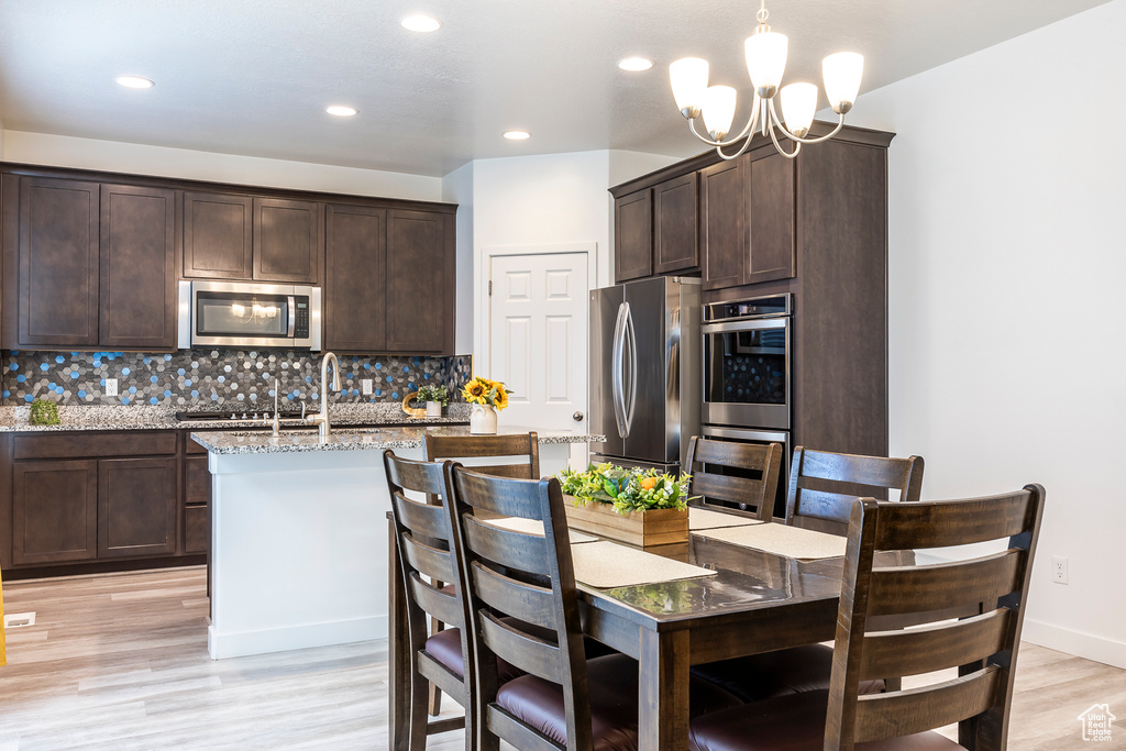 Kitchen featuring decorative backsplash, appliances with stainless steel finishes, dark brown cabinetry, and a chandelier