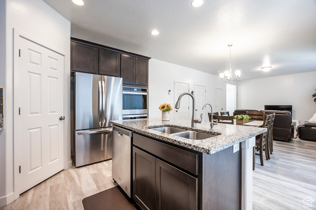 Kitchen with dark brown cabinetry, appliances with stainless steel finishes, an inviting chandelier, a sink, and open floor plan