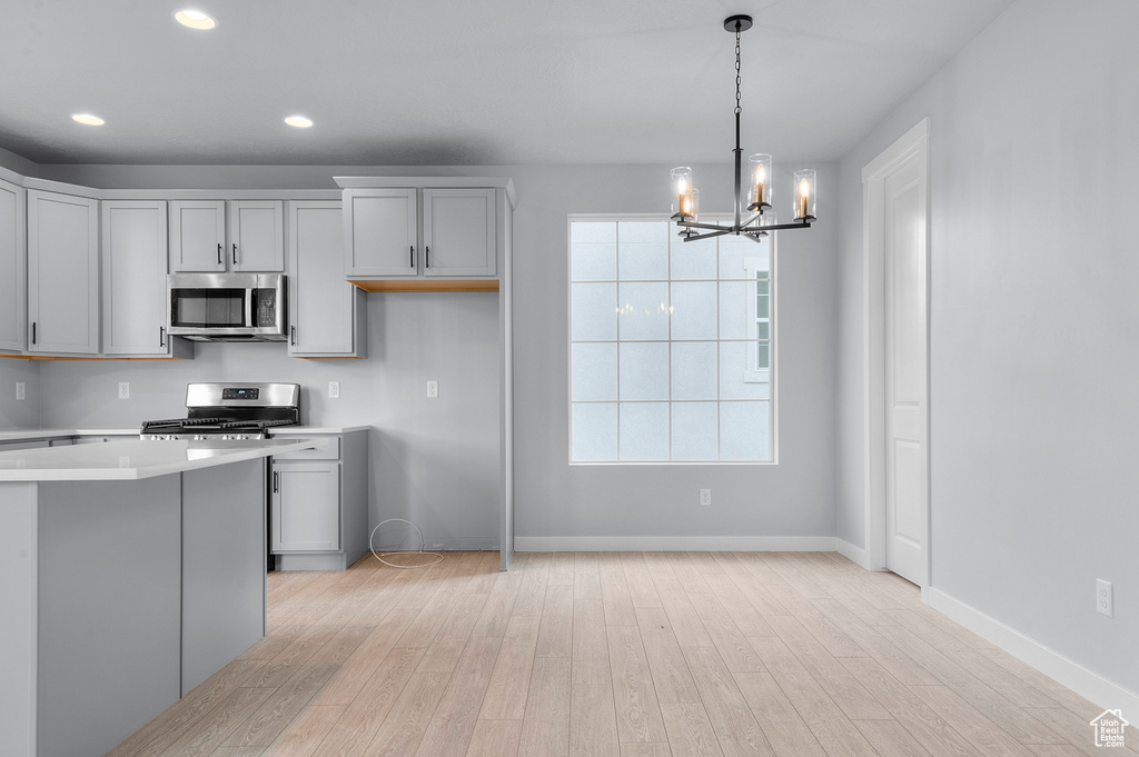 Kitchen featuring stainless steel appliances, a chandelier, light wood-style floors, light countertops, and hanging light fixtures