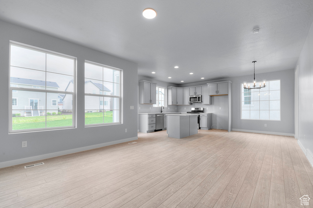 Kitchen featuring stainless steel appliances, baseboards, a chandelier, light wood finished floors, and open floor plan