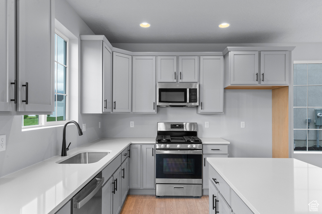 Kitchen with appliances with stainless steel finishes, a sink, light countertops, recessed lighting, and light wood-style floors