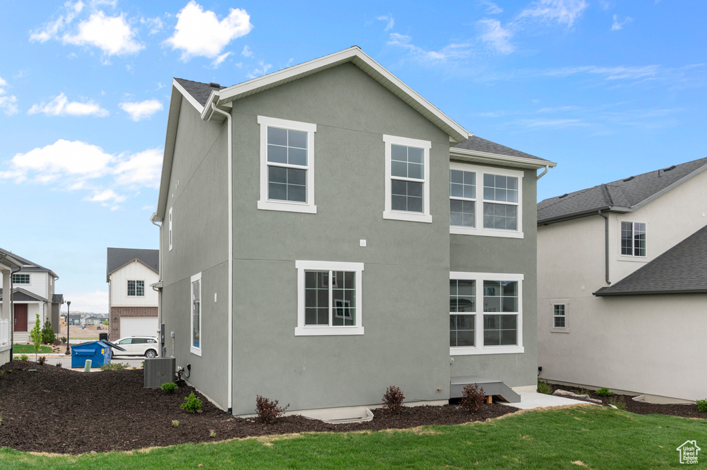 Back of house with stucco siding, a lawn, and central air condition unit