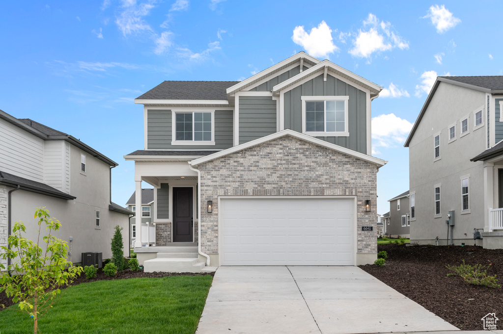 Craftsman-style house with board and batten siding, concrete driveway, a front lawn, and central air condition unit