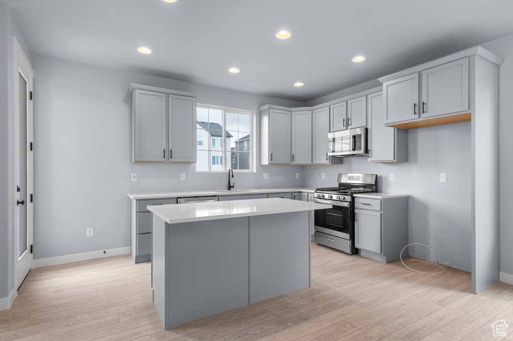Kitchen with stainless steel appliances, a sink, a center island, light wood-style flooring, and light countertops