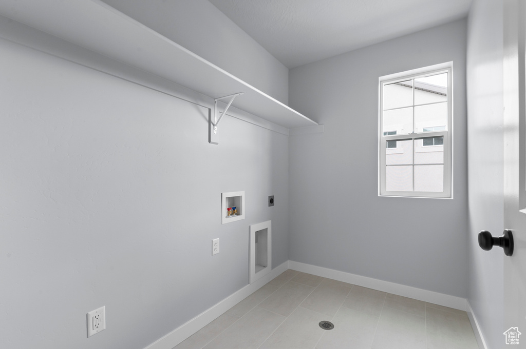 Clothes washing area with electric dryer hookup, hookup for a washing machine, baseboards, and light tile patterned floors
