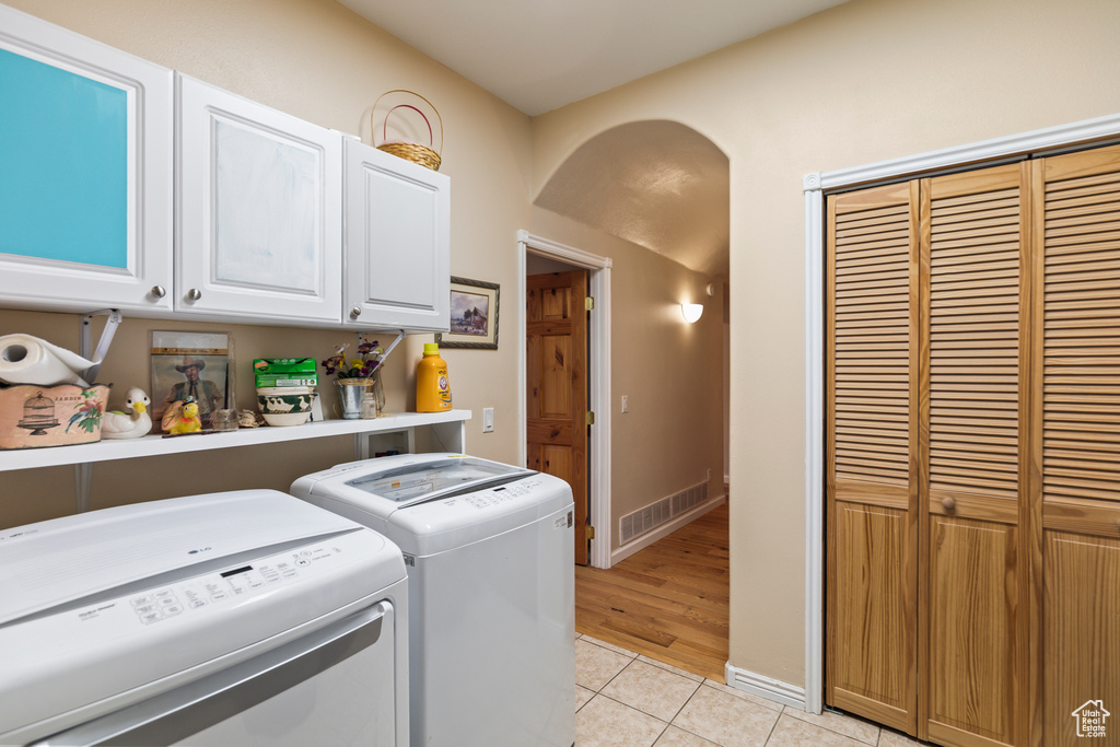 Washroom featuring cabinet space, washer and dryer, arched walkways, light tile patterned floors, and visible vents