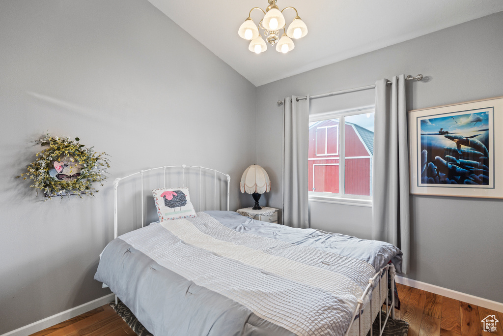 Bedroom featuring baseboards, lofted ceiling, wood finished floors, and a notable chandelier