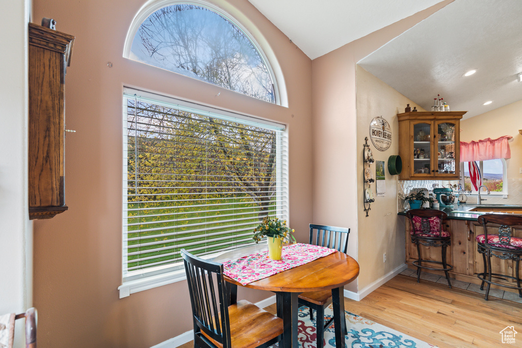 Dining area with baseboards, light wood finished floors, a healthy amount of sunlight, and vaulted ceiling