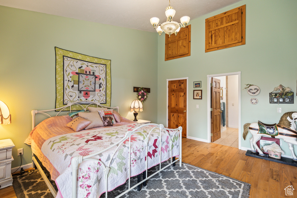 Bedroom with a towering ceiling, baseboards, wood finished floors, and a notable chandelier