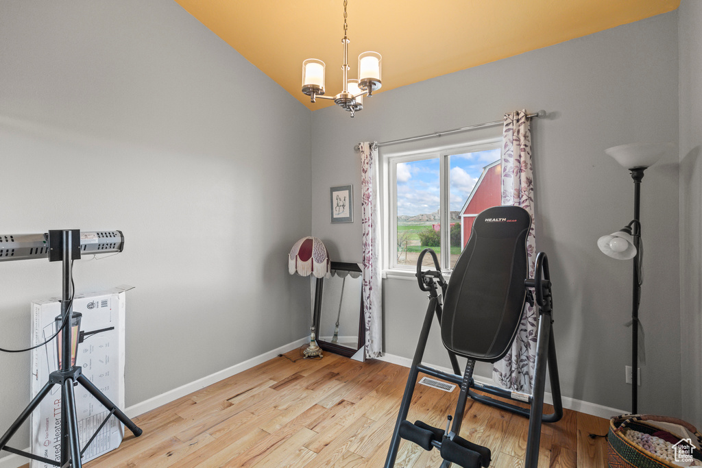 Workout room featuring baseboards, a chandelier, lofted ceiling, and light wood-type flooring