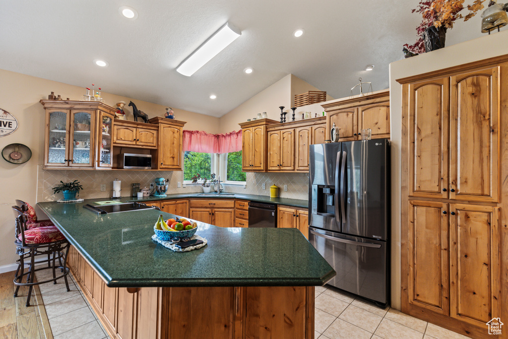 Kitchen with dark countertops, appliances with stainless steel finishes, backsplash, vaulted ceiling, and glass insert cabinets