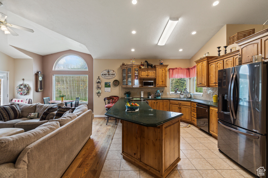 Kitchen featuring brown cabinetry, open floor plan, black appliances, and vaulted ceiling