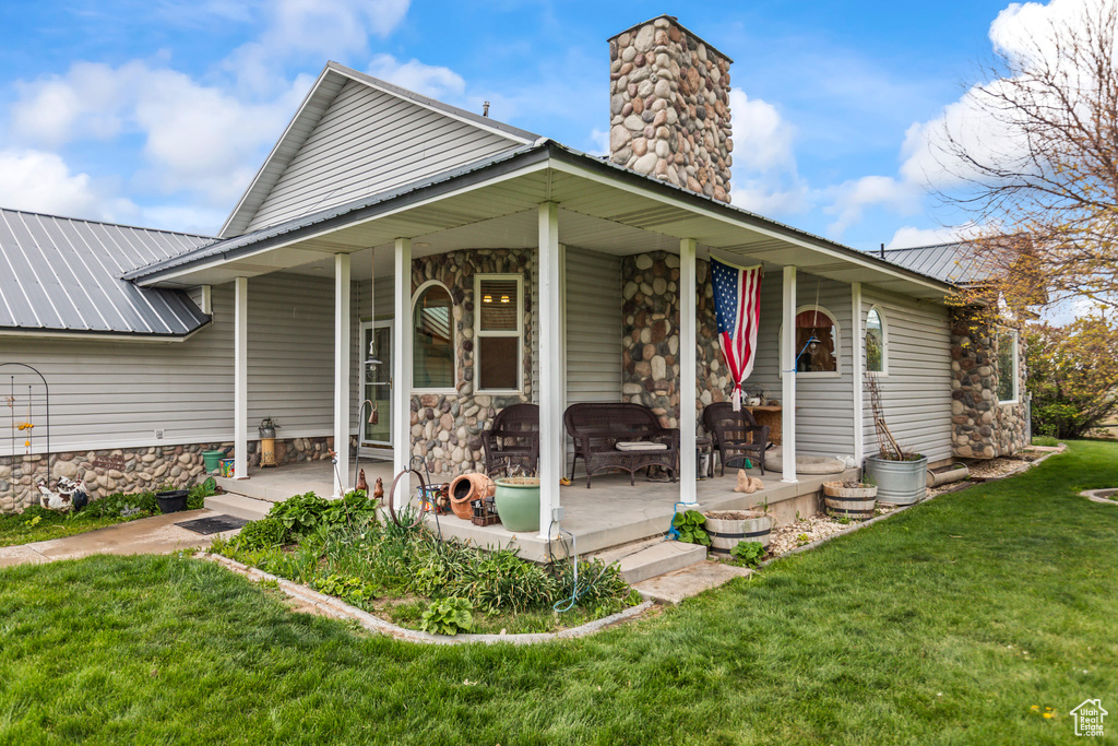 View of front of house featuring stone siding, a front yard, a chimney, covered porch, and metal roof