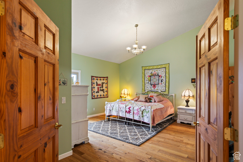 Bedroom with baseboards, a notable chandelier, vaulted ceiling, and wood finished floors