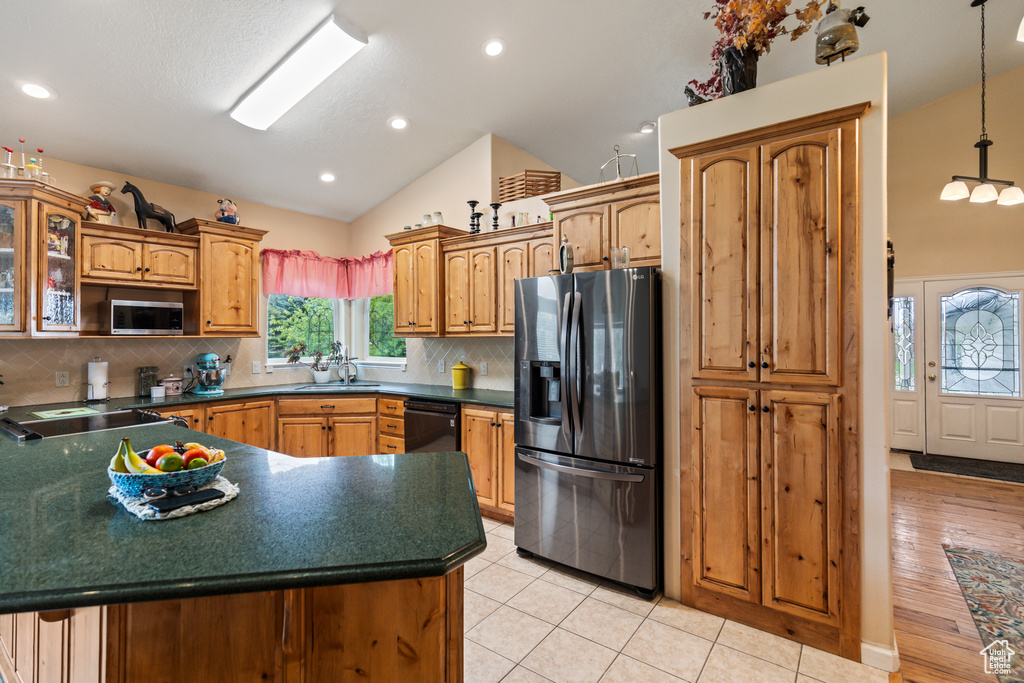 Kitchen featuring appliances with stainless steel finishes, dark countertops, a sink, lofted ceiling, and glass insert cabinets
