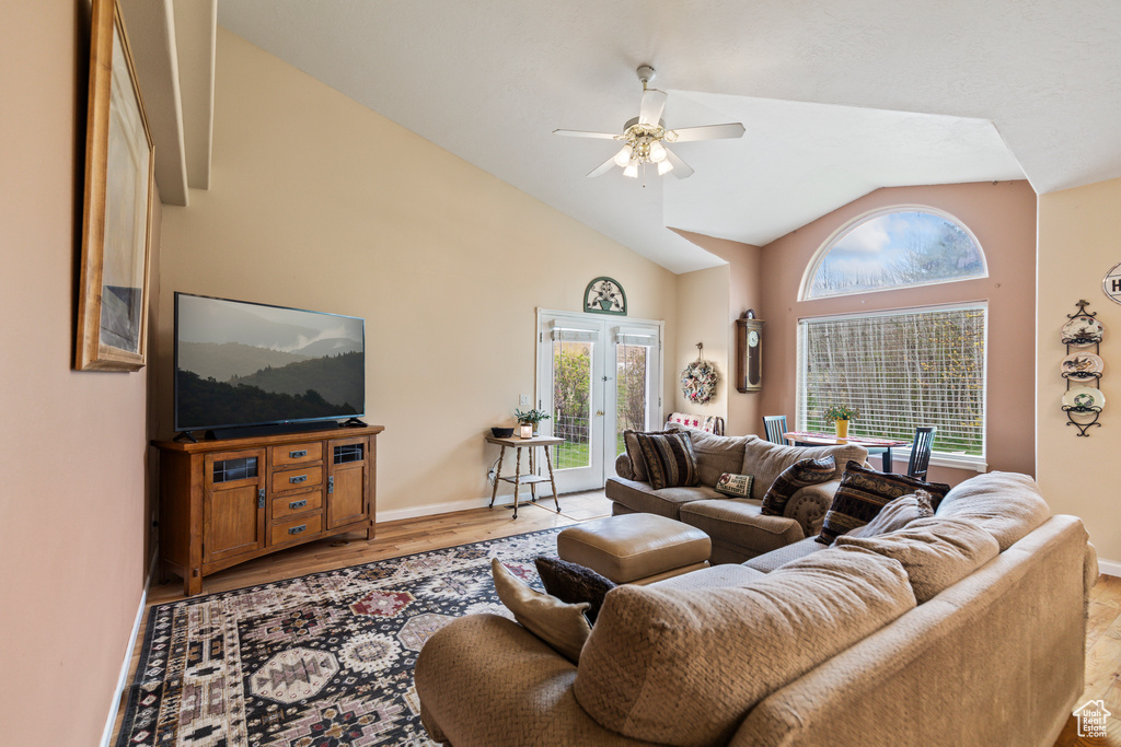 Living room featuring baseboards, ceiling fan, high vaulted ceiling, and light wood-type flooring