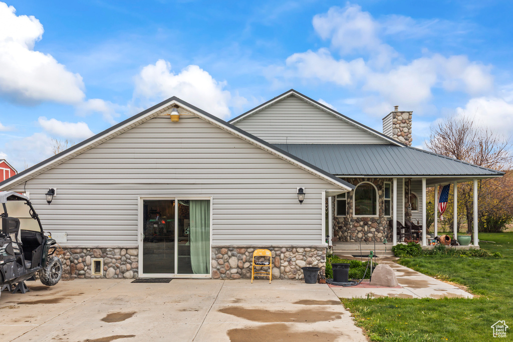 Rear view of property with covered porch, a chimney, a yard, and stone siding