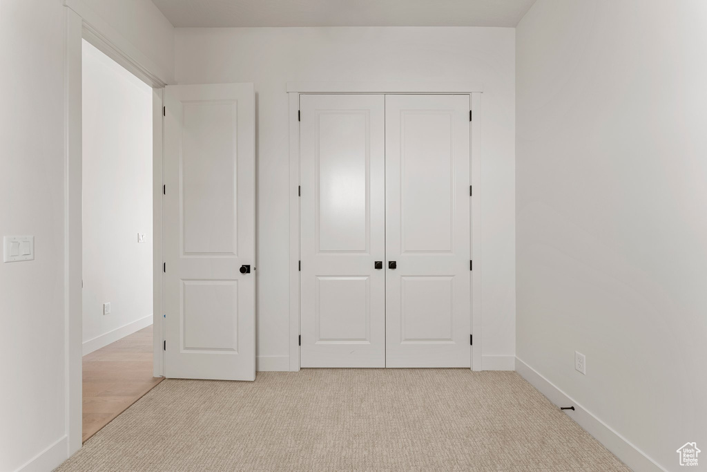 Unfurnished bedroom featuring baseboards, light carpet, and a closet
