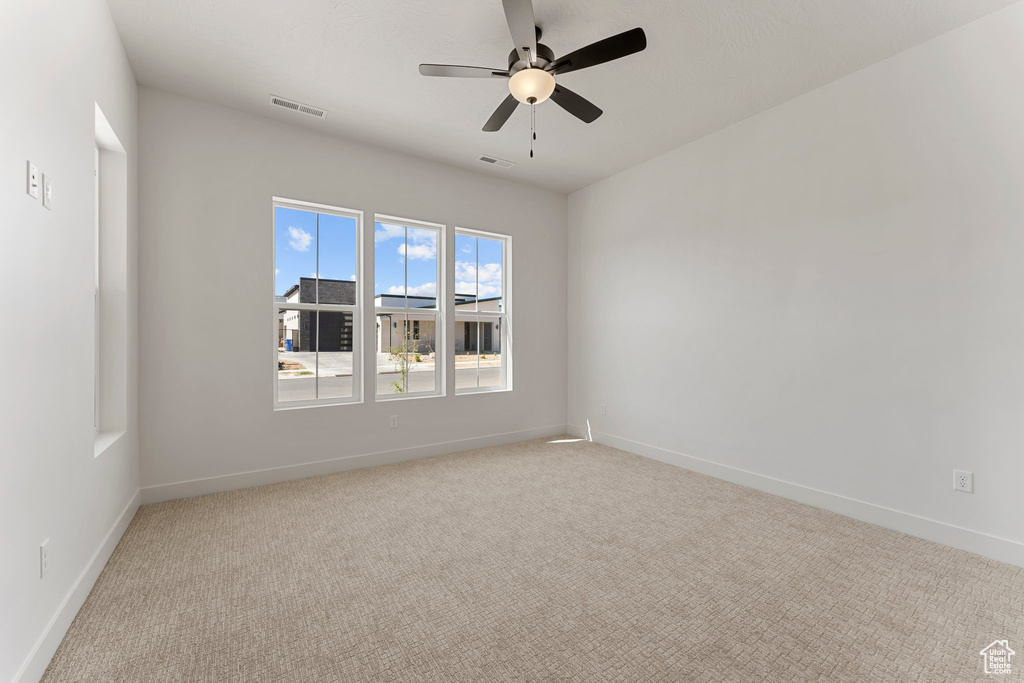 Empty room with baseboards, ceiling fan, visible vents, and light colored carpet