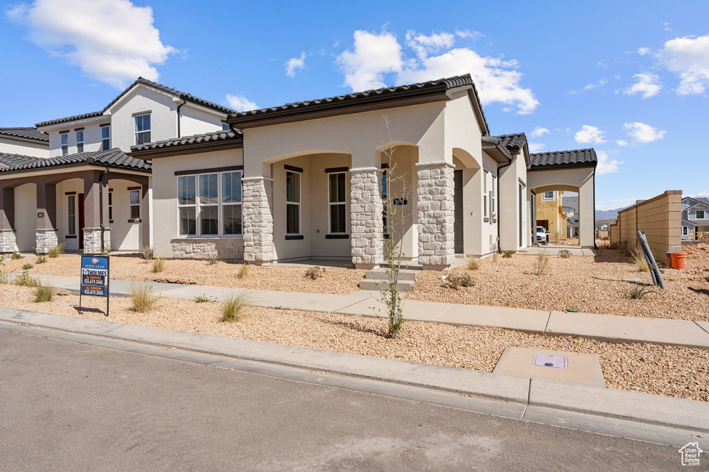 View of front of property featuring stucco siding, a tile roof, stone siding, and covered porch