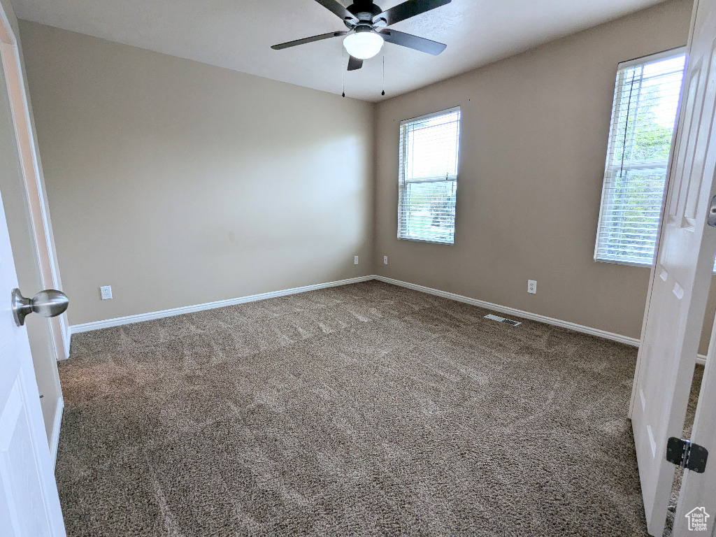Carpeted empty room with visible vents, a ceiling fan, and baseboards