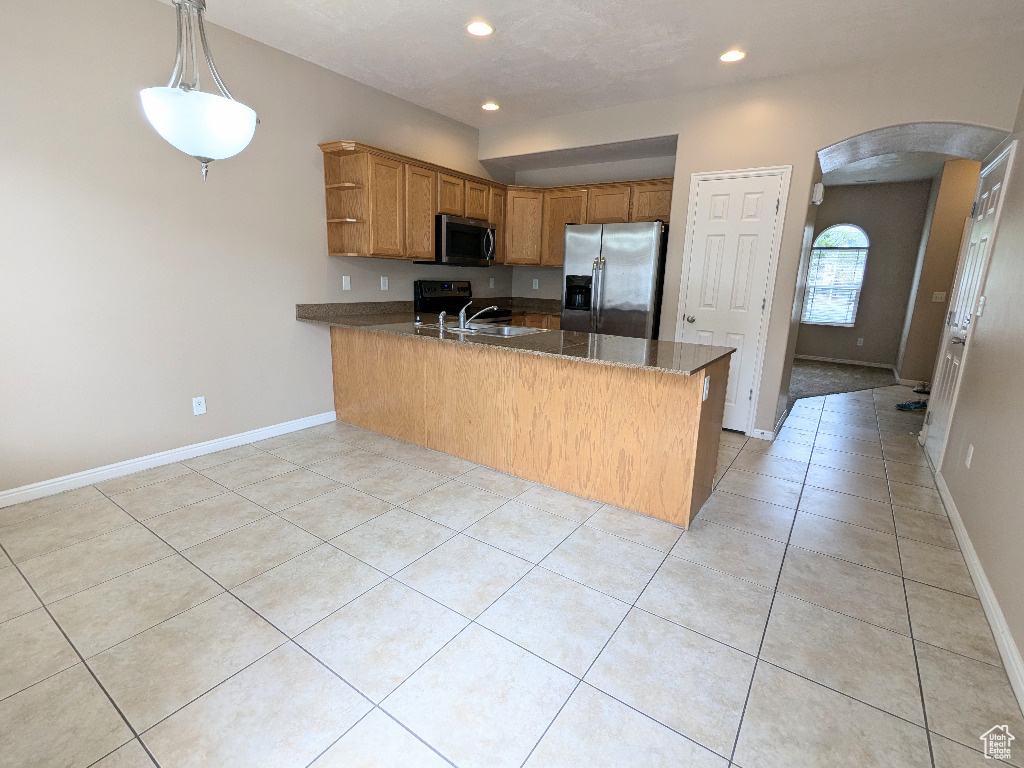 Kitchen featuring brown cabinetry, arched walkways, a peninsula, stainless steel appliances, and recessed lighting