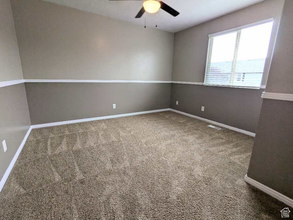 Carpeted spare room featuring baseboards, a ceiling fan, and visible vents