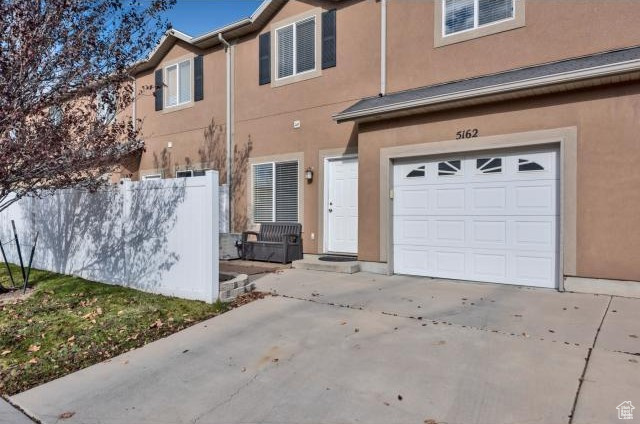 View of front of property featuring fence, an attached garage, concrete driveway, and stucco siding
