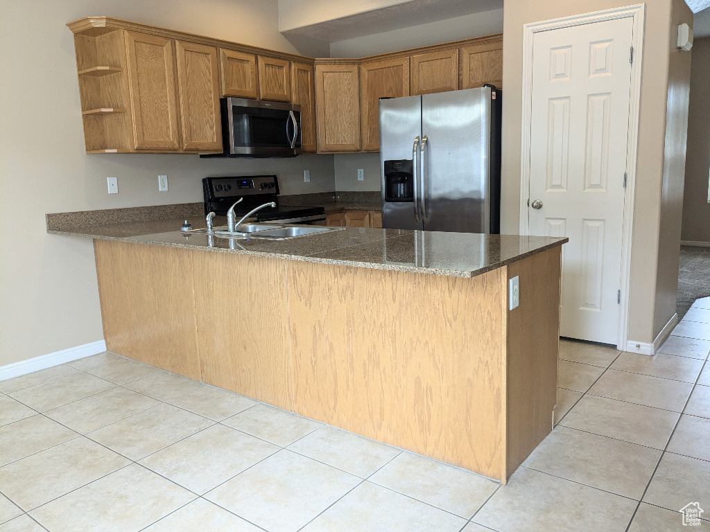Kitchen with brown cabinets, light tile patterned floors, a peninsula, dark stone counters, and stainless steel appliances