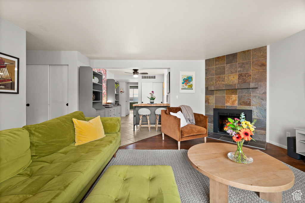 Living area featuring ceiling fan, visible vents, a tiled fireplace, and wood finished floors