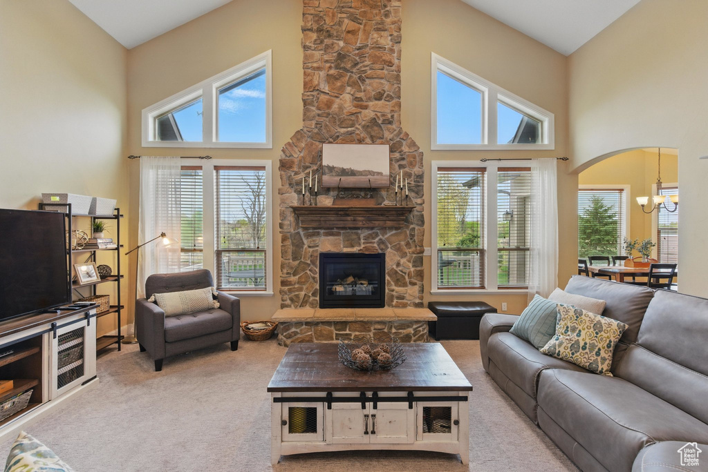 Carpeted living room featuring plenty of natural light, a towering ceiling, a chandelier, and a stone fireplace