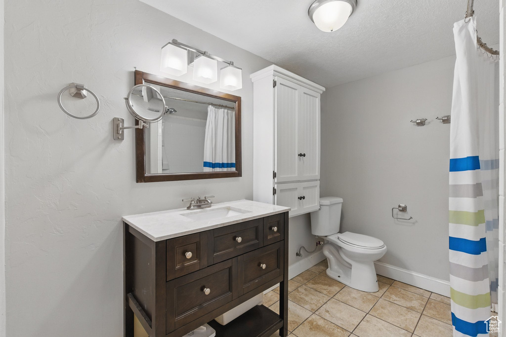Bathroom featuring tile patterned flooring, vanity, toilet, baseboards, and curtained shower