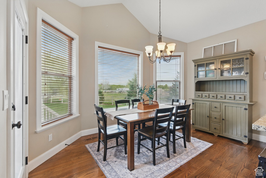 Dining space with baseboards, an inviting chandelier, dark wood-style floors, and vaulted ceiling