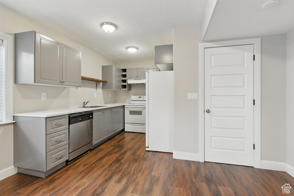 Kitchen featuring baseboards, gray cabinetry, under cabinet range hood, and white appliances
